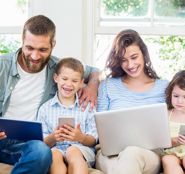 familia el el sofá con dispositivos electrónicos, algo que podría provocarles adormecimiento de manos